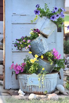 some flowers are growing in buckets on the side of a building with a blue door