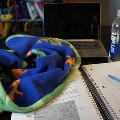 a laptop computer sitting on top of a desk next to a blue and green blanket