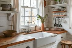 a kitchen with white cabinets and wooden counter tops next to a window filled with potted plants