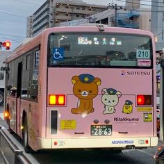 a pink bus driving down a street next to tall buildings and traffic lights in japan