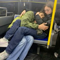 two people are sleeping on a public transit bus with their arms around each other as they hug