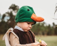 a small child wearing a green duck hat and holding a branch in his hands while standing on the grass