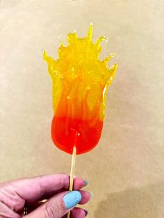 a hand holding a lollipop with orange and yellow jelly on it