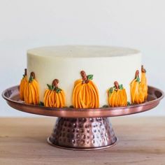 a cake decorated with pumpkins and leaves on a metal platter sitting on a wooden table