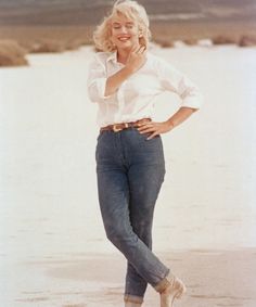 a woman standing on the beach with her hands in her pockets and smiling at the camera