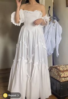 a woman in a white dress is taking a selfie with her cell phone while standing next to a suitcase