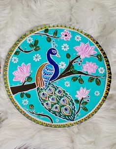 a peacock painted on a blue plate with flowers and leaves around the edge, sitting on a white furnishing