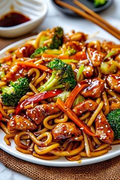 a white plate topped with chicken and broccoli covered in sauce next to chopsticks