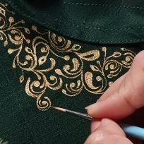 a person with a pen in their hand next to a green shirt that has gold designs on it