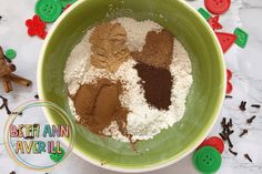 a green bowl filled with different types of spices on top of a white table next to buttons