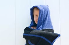 a young boy wrapped in a blue and black towel with his face peeking through the hood