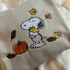 a snoopy dog with autumn leaves and pumpkins on it's face is embroidered onto the side of a pillow