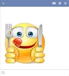 an emoticive smiley face holding a knife and fork with its tongue sticking out