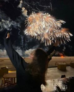 a woman is holding her arms up as fireworks go off in the sky