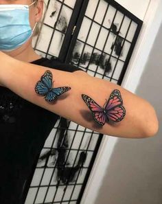 a woman wearing a face mask and holding up her arm with two butterflies on it