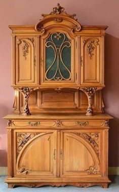 an old fashioned wooden cabinet with ornate carvings on the front and sides, against a pink wall