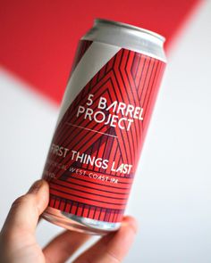 a hand holding a can of beer in front of a red and white striped background