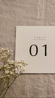 a table number is displayed next to some flowers on a linen covered tablecloth,