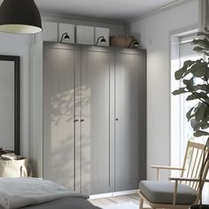 a bedroom with a bed, chair and cupboards in the corner next to a window