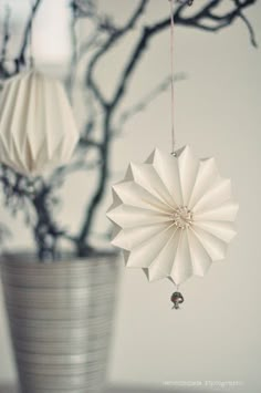 two white origami ornaments hanging from a tree branch in a potted plant