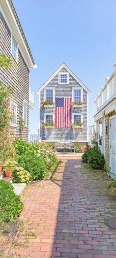 an american flag hanging from the side of a house on a brick walkway in front of some houses