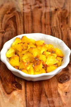 a white bowl filled with sliced pineapple on top of a wooden table next to a knife