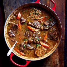 a red pot filled with stew on top of a wooden table