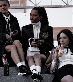 three young women sitting on steps with cell phones in their hands and one holding a purse