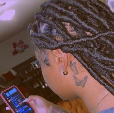 a woman with dreadlocks is looking at her cell phone and has tattoos on her arm