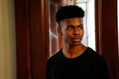 a young man with black hair standing in front of a door and looking at the camera