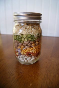 a glass jar filled with lots of food on top of a wooden table next to a wall