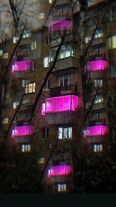 an apartment building lit up with pink lights in the window sill and tree branches