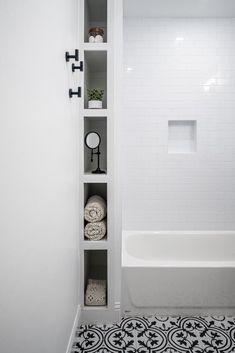 a white bathroom with black and white flooring, shelving unit and bathtub