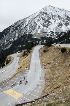 two people riding their bikes down the road in front of a snow - capped mountain