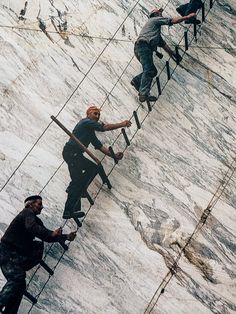 three men climbing up the side of a snow covered mountain