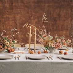 the table is set with white plates, silverware and floral centerpieces on it