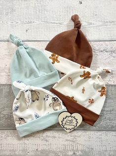 three baby hats on top of a wooden table next to a heart ornament