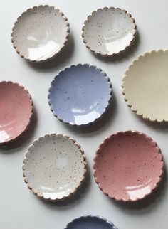 six different colored dishes with scalloped rims on white table top next to each other