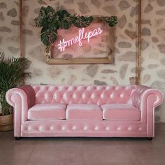 a pink couch sitting in front of a wall with a neon sign on it's side