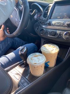 two cups of coffee sit on the dashboard of a car, while someone is driving