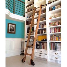 there is a ladder in the room with many books on shelves and below it are white drawers