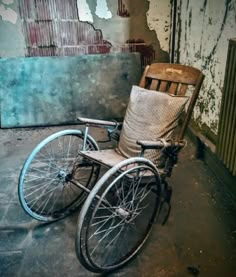 an old wooden chair sitting on top of a floor next to a dirty wall with peeling paint