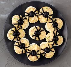 a black plate topped with devil's eggs covered in cheese and black spider magnets