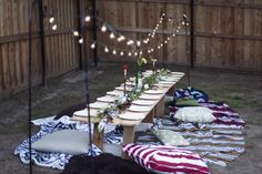 a long table set up in the middle of a yard with lights strung over it