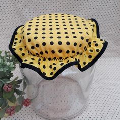 a yellow and black polka dot hat sitting on top of a glass vase next to a potted plant