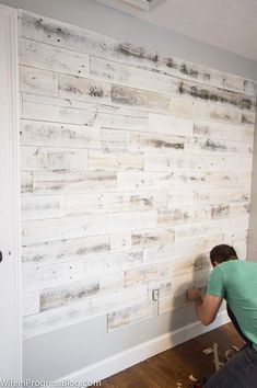 a man is painting a wooden wall with white paint and wood planks on it