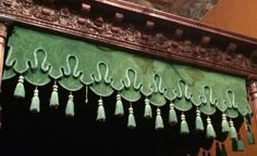 an ornate wooden frame with green tassels hanging from it's sides in front of a painting on the wall