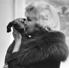 a woman kissing a small dog on the nose in a black and white photo with fur collar