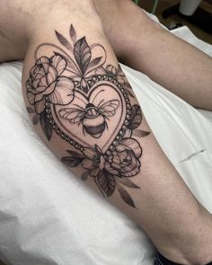 a heart tattoo with flowers and a bee on the side of his arm, sitting on a bed