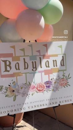 there is a sign that says babyland with flowers and balloons in the back ground